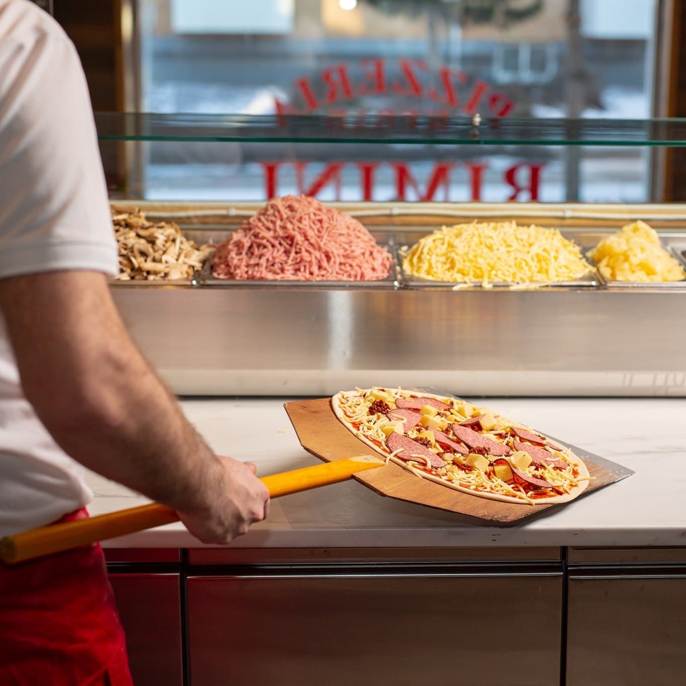 Nygjord pizza på pizzaspade vid topping-baren hos Pizzeria Rimini